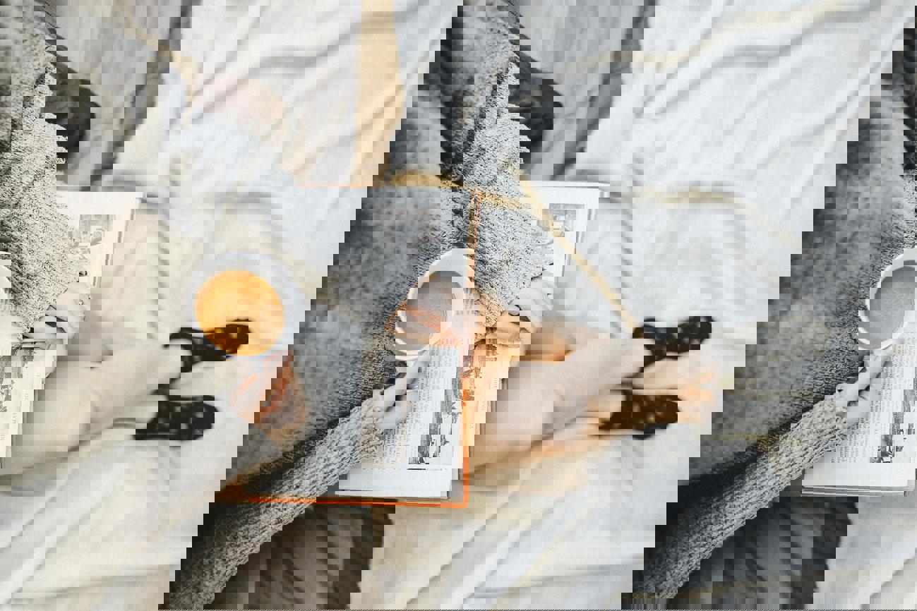 Reading a book in bed whilst holding a coffee