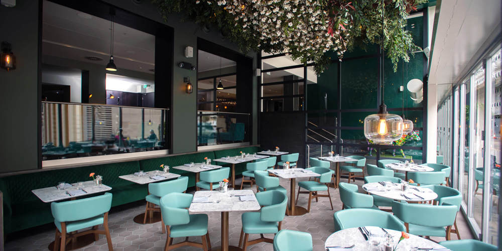 Tables and chairs set up under the floral canopy at The Lampery